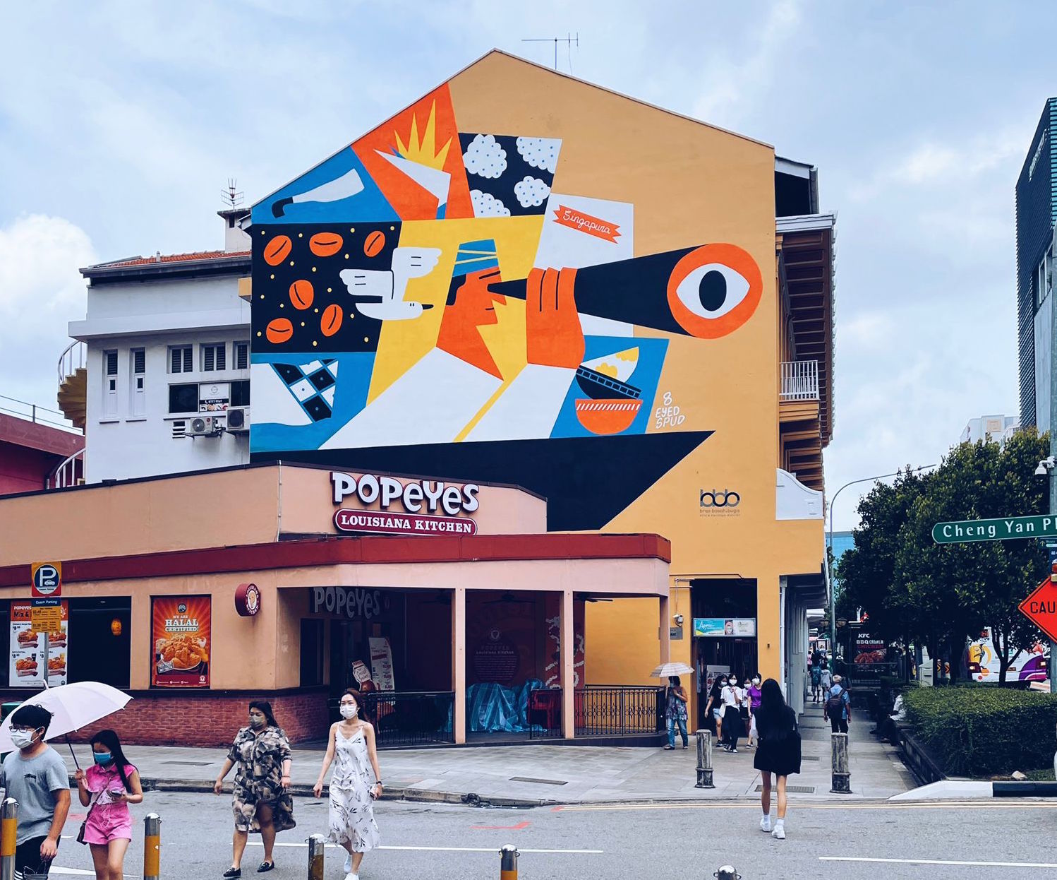 A large public mural commissioned by Bras Basah.Bugis on a precinct shophouse wall, with pedestrians passing below